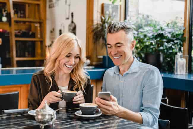 Amour et relation. Heureux couple mature romantique buvant du café au café-restaurant à une date tandis que le mari montre à sa femme quelque chose sur le téléphone intelligent.